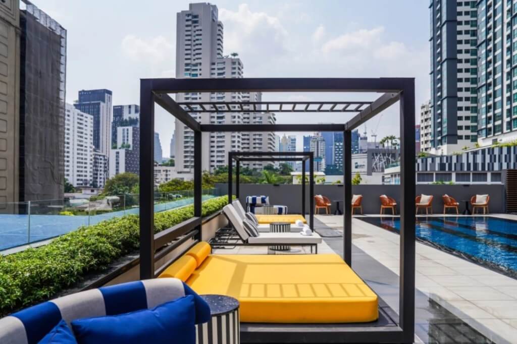 Tribe Living Bangkok Sukhumvit 39 rooftop pool area with sun loungers and bed, perfect for relaxing in the evening breeze