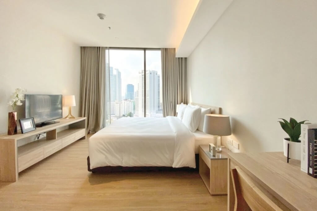 Oakwood Suites Bangkok double bedroom with wooden bed frame and TV cabinet