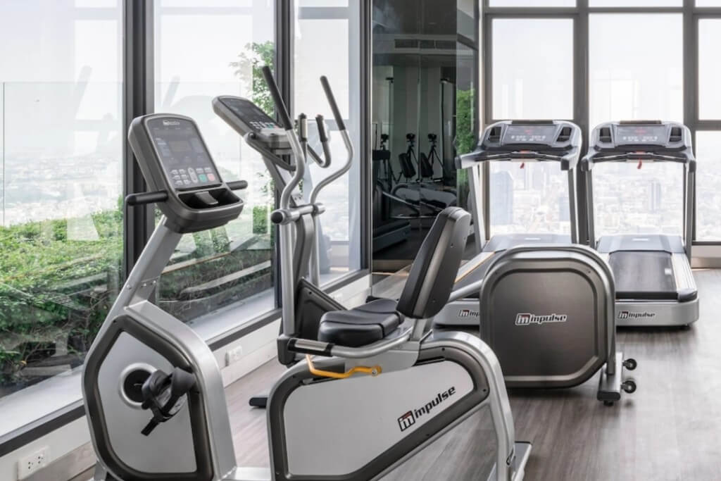 Spacious gym with floor-to-ceiling windows next to swimming pool at Ramada Plaza Bangkok