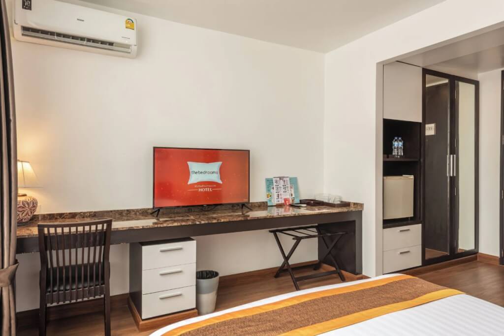 Guest room interior with TV, luggage rack, vanity desk, and mini fridge