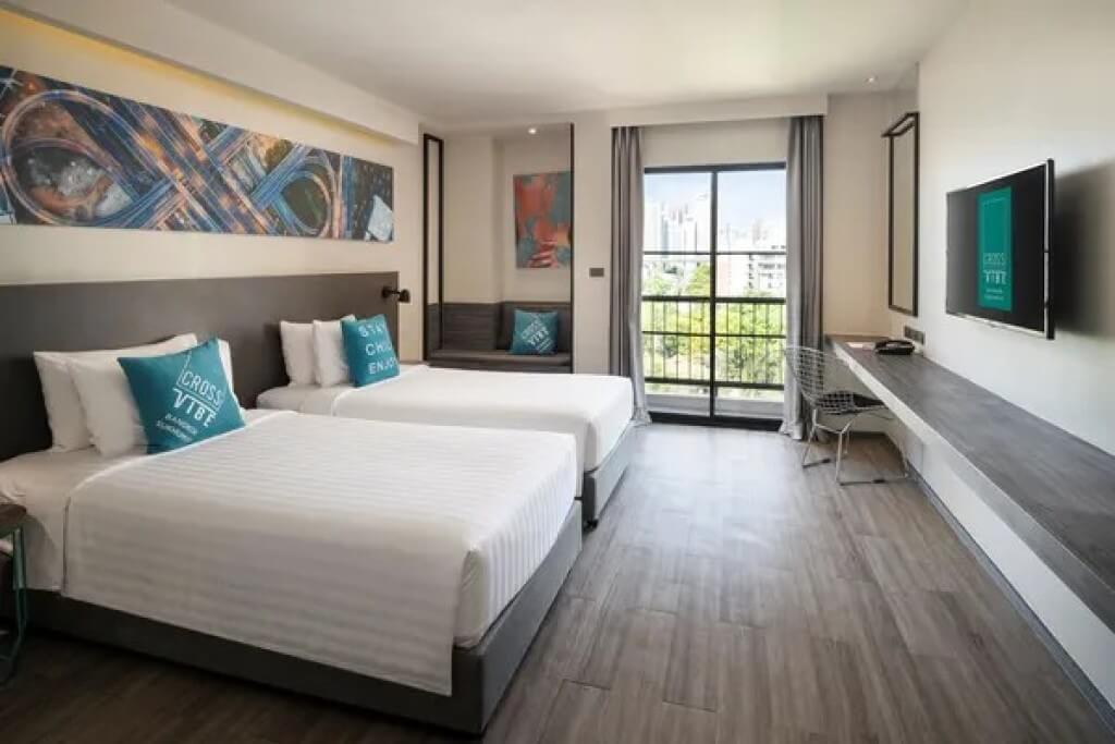 Cross Vibe Bangkok Sukhumvit twin room view from entrance door looking toward twin beds and full-length window with city daylight